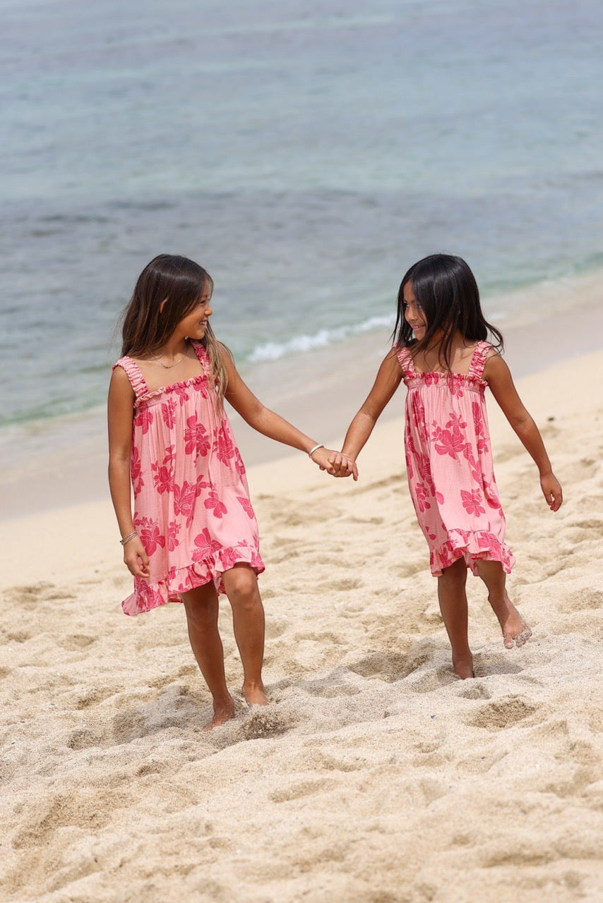Guava Jammies Mahealani Mini Dress in pink with red floral print, featuring ruffled straps and hem. Two girls on a beach.