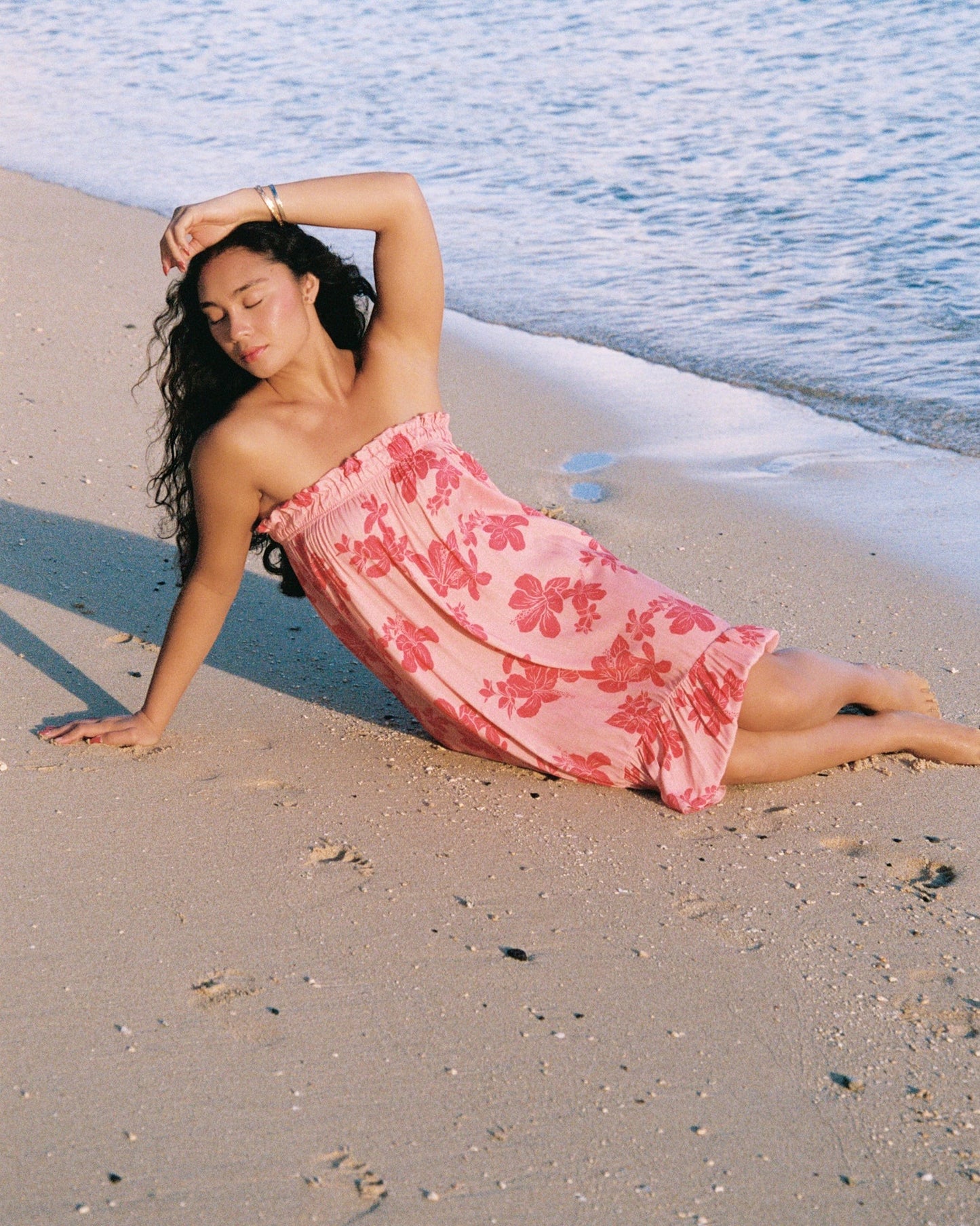 Guava Jammies pink floral strapless midi dress with elastic top and high-low hem, worn by a model on a beach.